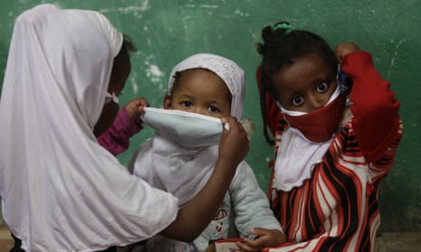 A child helps a friend put on a face mask as a precaution against coronavirus.