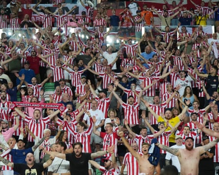Sunderland fans in red and white striped jerseys cheer with arms raised at a match