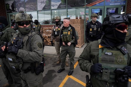 Men in military clothing and masks stand around a gas station.
