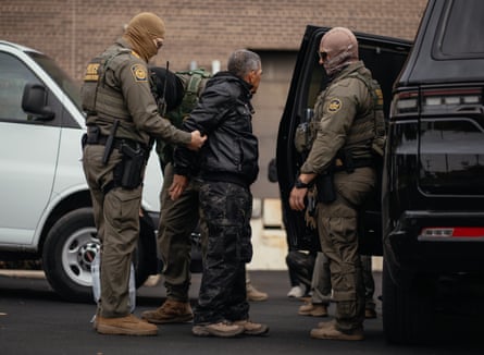 A man is shown being handcuffed by agents in uniform wearing full face mask