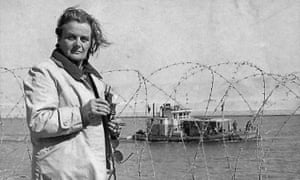 Clare Hollingworth stands in front of barbed wire with a ship in the background