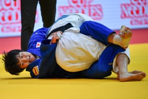 Two women locked in a judo hold on a yellow mat