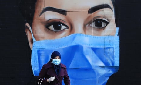 Woman in a face mask in front of a NHS mural