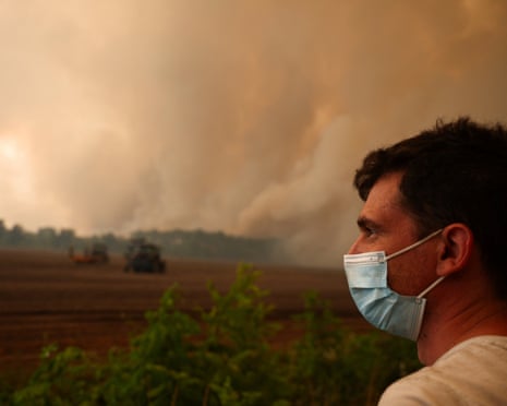 A man wears a mask, while smoke rises from a wildfire in Pierroton, Gironde, France.