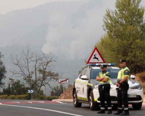 Civil Guards are seen on guard at a closed road as smoke raises from the wild fire very close to the Santa Barbara chapel at La Vall d’Uixo in Castellón, Spain.