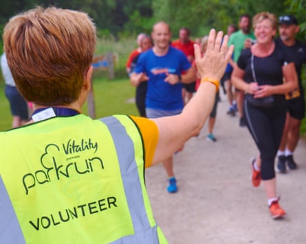 A parkrun volunteer waves to runners as they pass.