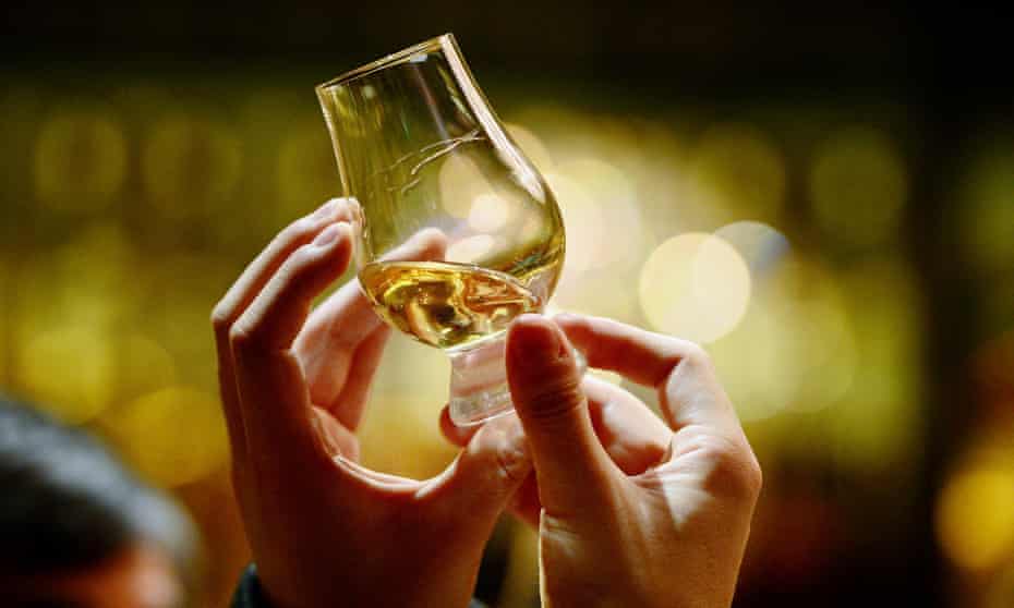 A person holds up a glass of whisky
