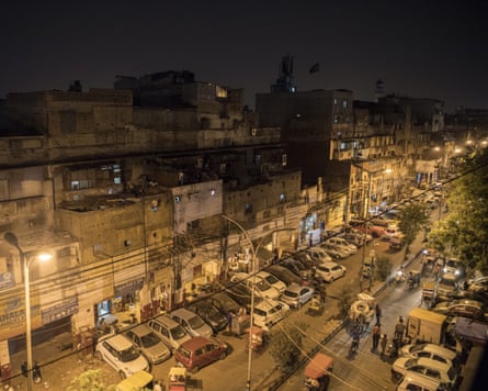 A busy street in Delhi lined with cars and people