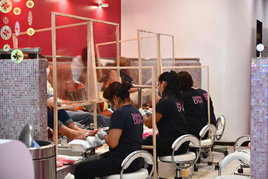 Women wearing black shirts that say “Dashing Diva” on the back in hot pink lettering work at pedicure stations inside a nail salon.