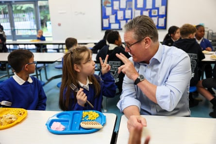 Keir Starmer holds up two fingers to a girl doing the same to him in a primary school classroom