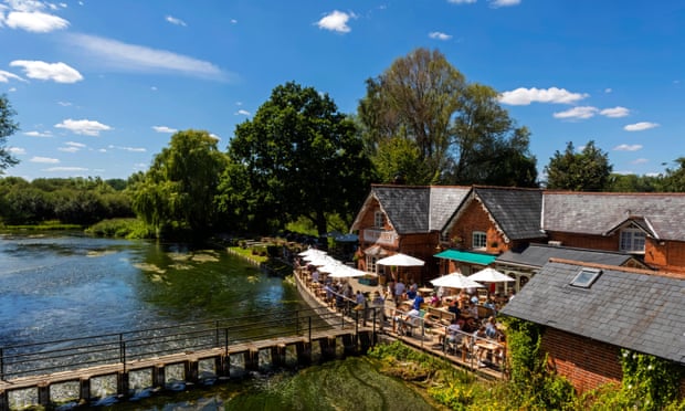A sunny day at the Mayfly Pub with its terrace with tables and umbrellas overlooking a weir