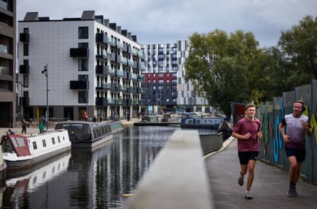 Two men jog along New Islington’s canal path beside moored narrowboats and modern apartments