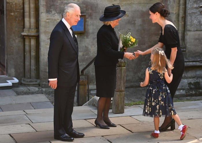 King Charles looks on as the Queen Consort receives flowers from a young girl accompanied by her mother outside Llandaff Cathedral.
