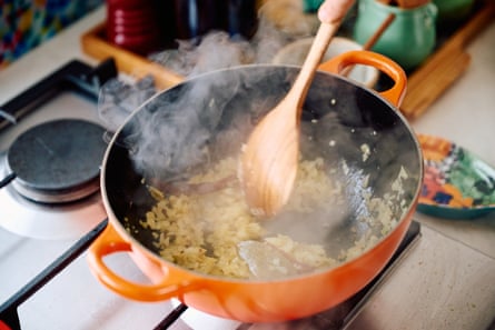 A hand stirring chopped onions cooking in a pot.