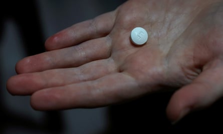 A hand holds a white pill.