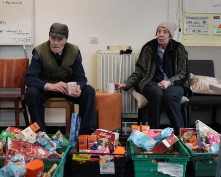 Two people in a community centre with crates of food.