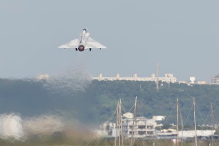 The fighter jet viewed from behind as it soars into the air above trees and buildings