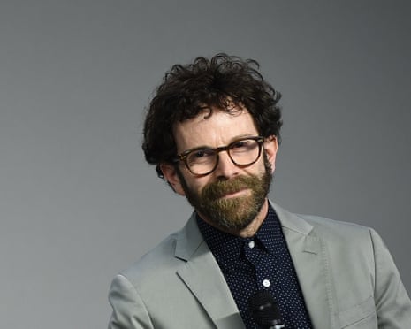 Charlie Kaufman in thick rimmed glasses, bearded wearing black shirt, grey jacket.