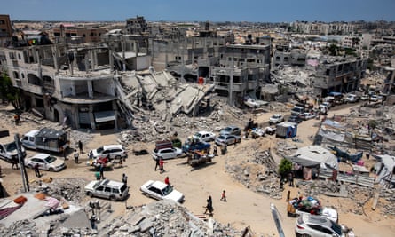 People standing in a street filled with cars and other vehicles amid the ruins of bombed-out buildings.