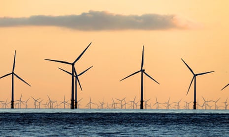 Wind turbines that are part of a wind farm are seen from a beach at sunset.