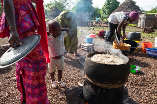 Women cook large pots of fonio over open fires outside their huts