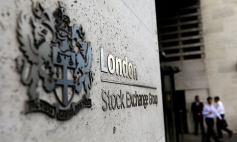 The London Stock Exchange sign on a grey building located in the City of London. A group of employees stand nearby, on the right hand side.
