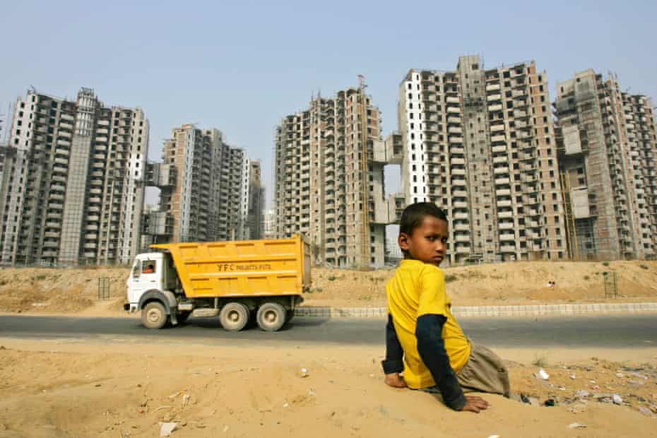 A boy sits with the backdrop of a residential complex in Gurgaon, India