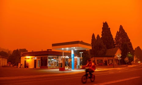 A man rides his bike past a gas station as smoke fills the sky in Greenville, California last week. The Dixie fire has become the largest in California after it exploded in size over the weekend.