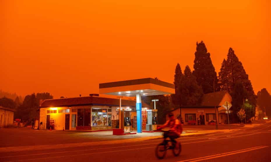 A man rides his bike past a gas station as smoke fills the sky in Greenville, California last week. The Dixie fire has become the largest in California after it exploded in size over the weekend.