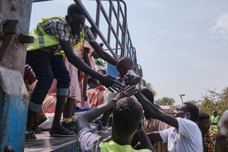 A baby is held up to a man wearing a hi-vi vest standing on a high sided truck