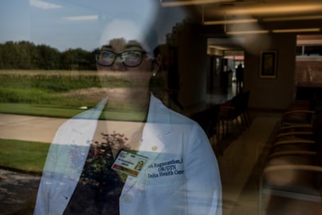 Woman in a white coat wearing glasses looks out a window reflecting the outside