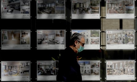 a man with a face mask passes an estate agent window