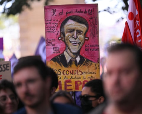 Protesters hold a placard depicting a caricature of Emmanuel Macron with earplugs sticking out of his ears