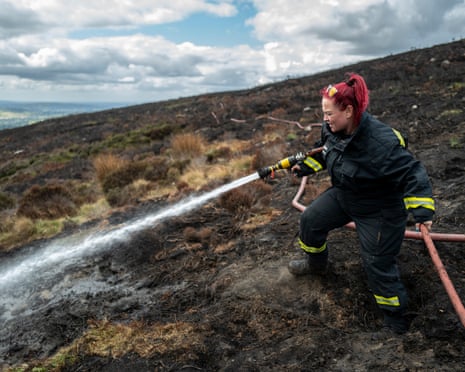 Firefighter Bev sprays water from a hose across charred moorland after a wildfire