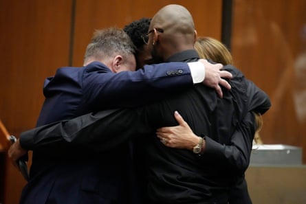 Four people embrace in a group hug in a courtroom.