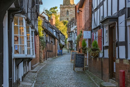A curved narrow street with Tudor buildings either side and a church tower at the end