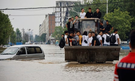 People ride a front loader as they make their way through a flooded road following heavy rainfall in Zhengzhou, Henan province