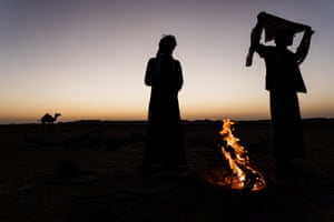 Bedouin men stand at their campfire at dusk