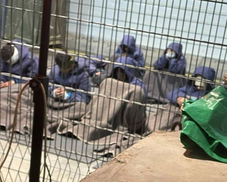 Palestinian prisoners sit on the floor behind bars, some blindfolded or with hoods up