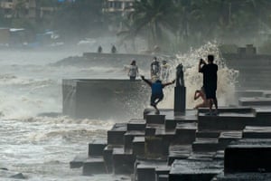 People take pictures on a promenade as waves hit the coast during monsoon rains