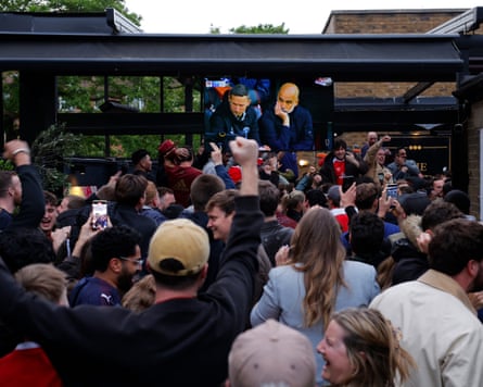 Fans hold their hands in the air after seeing a Bournemouth goal on a TV in a pub garden