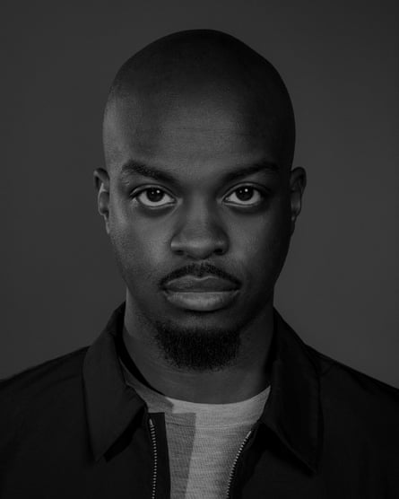 Monochrome portrait of George the Poet wearing a dark collarless jacket and light T-shirt against a dark grey background