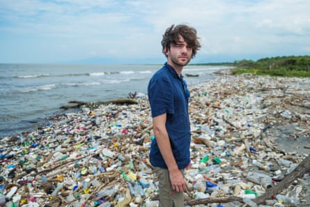 Boyan Slat standing in front of a mound of waste and plastic bottles washed up on a beach