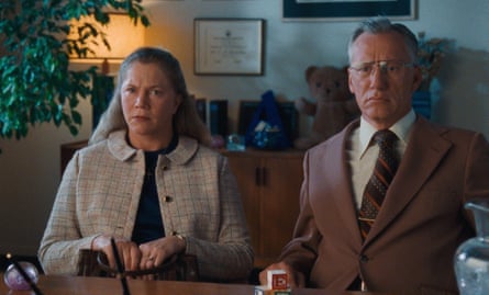 A man and a woman sit at a desk in an office looking perplexed