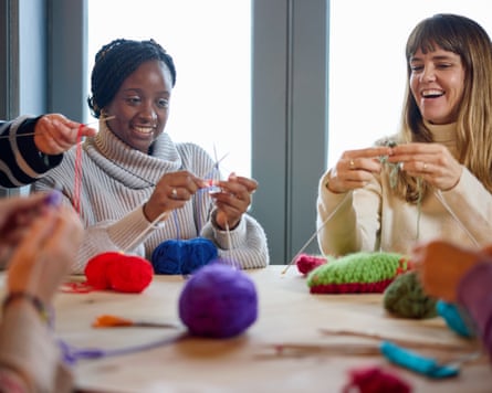Happy group of friends enjoying craft workshop sitting at wooden table in cafe learning knitting with balls of wool