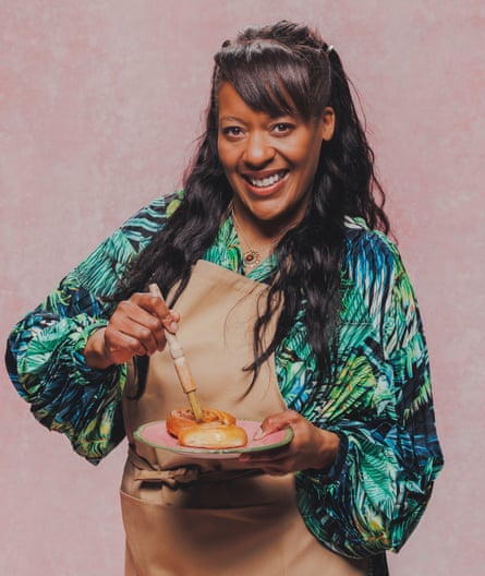 A black woman with a fringe and patterned blouse coats a pastry with a wash.