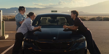All three lean on a car with hills in the background