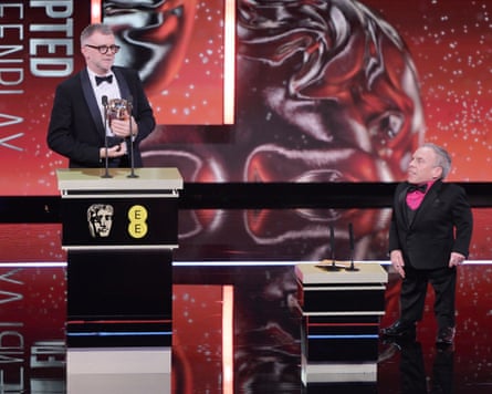 Warwick Davis, with mini lectern, speaks with Paul Thomas Anderson as he accepts the best adapted screenplay award.