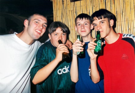 The four boys stand shoulder to shoulder, with three of them holding up bottles of beer