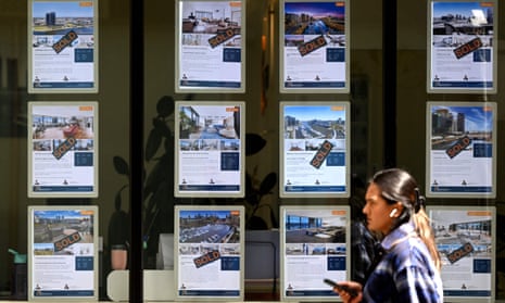 Woman walks past real estate agent shopfront with property listings in the window